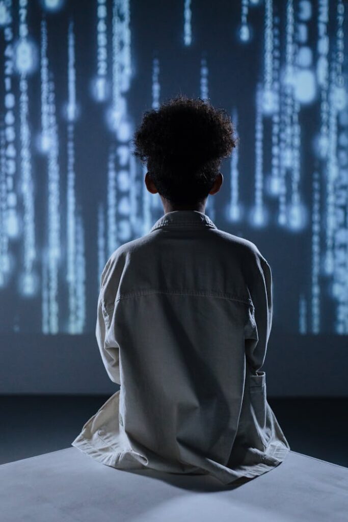 pexels-photo-9783350 Back view of a child sitting and facing a digital display, evoking technological themes.